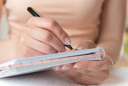 Tight shot of women's hands writing a note on a notepad.