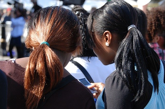 Over-the-shoulder shot of two teenage girls who are sharing smart phone messages, illustrating basic interpersonal communication.